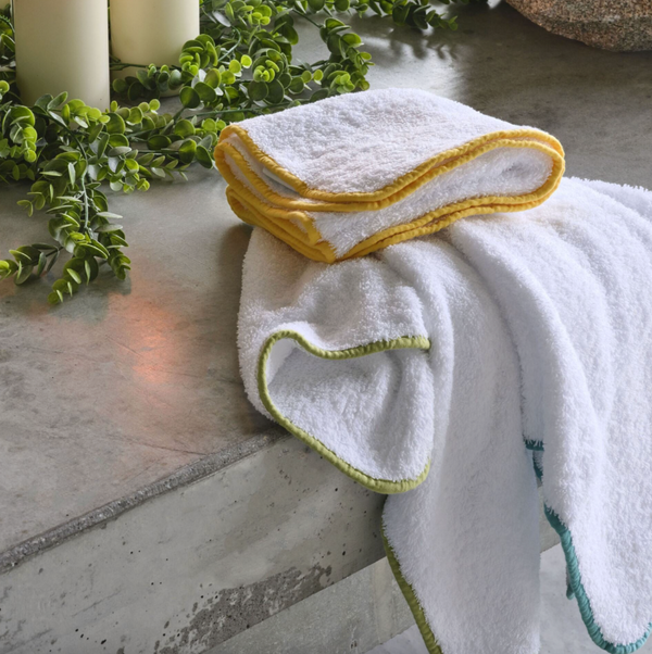White terry towels with yellow and green contrast borders, styled on stone surface.