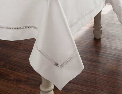 Doric white linen tablecloth with hemstitch border draped over dining table.
