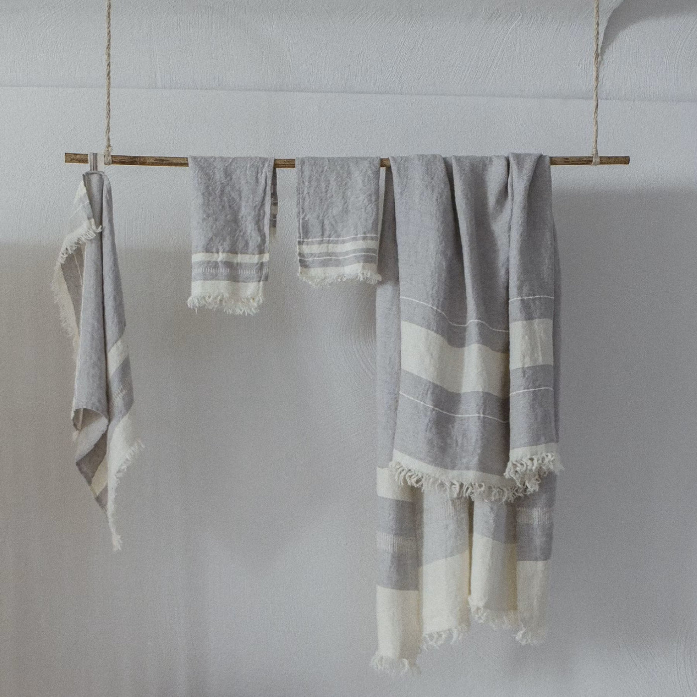 Striped towels hang from a wooden deck above a sandy beach, with a basket nearby and a sailboat visible in the distance on the water.