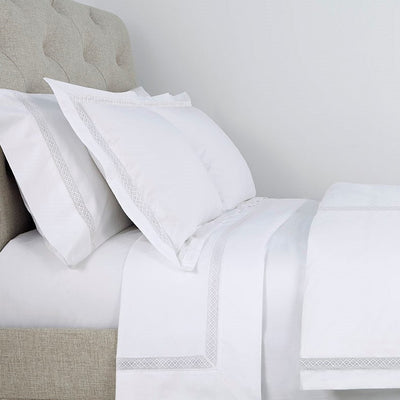 Sferra Valencia white bedding with silver embroidered border on bed with linen headboard.