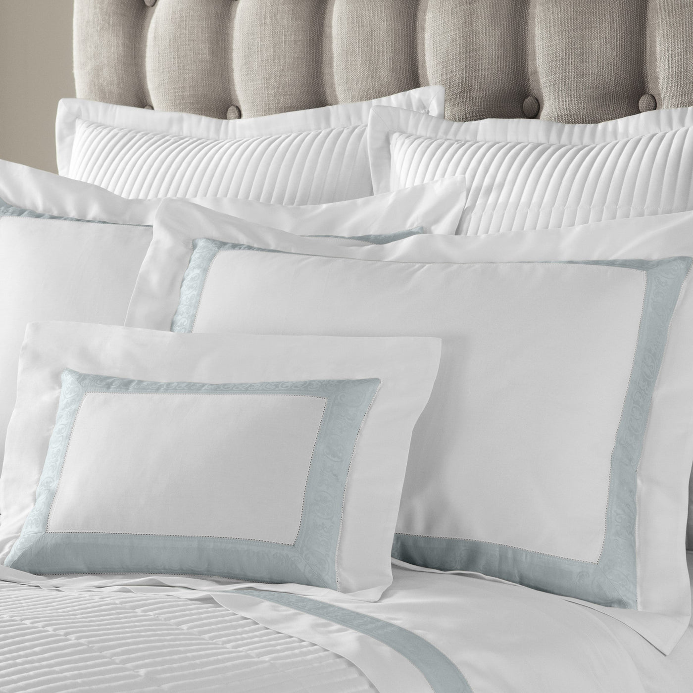 Sferra Venice white bedding with pale aqua border, styled on upholstered bed.