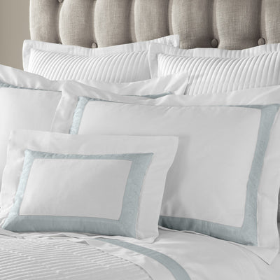 Sferra Venice white bedding with pale aqua border, styled on upholstered bed.