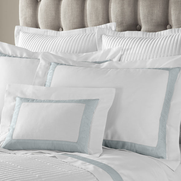 Home Treasures Venice white bedding with pale aqua border, styled on upholstered bed.