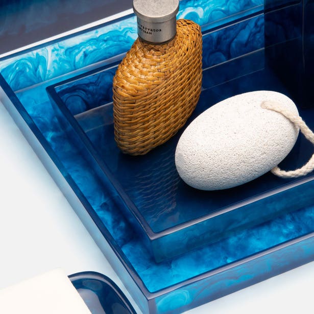 Blue resin marbled nesting trays styled with woven bottle and pumice stone, angled close-up.