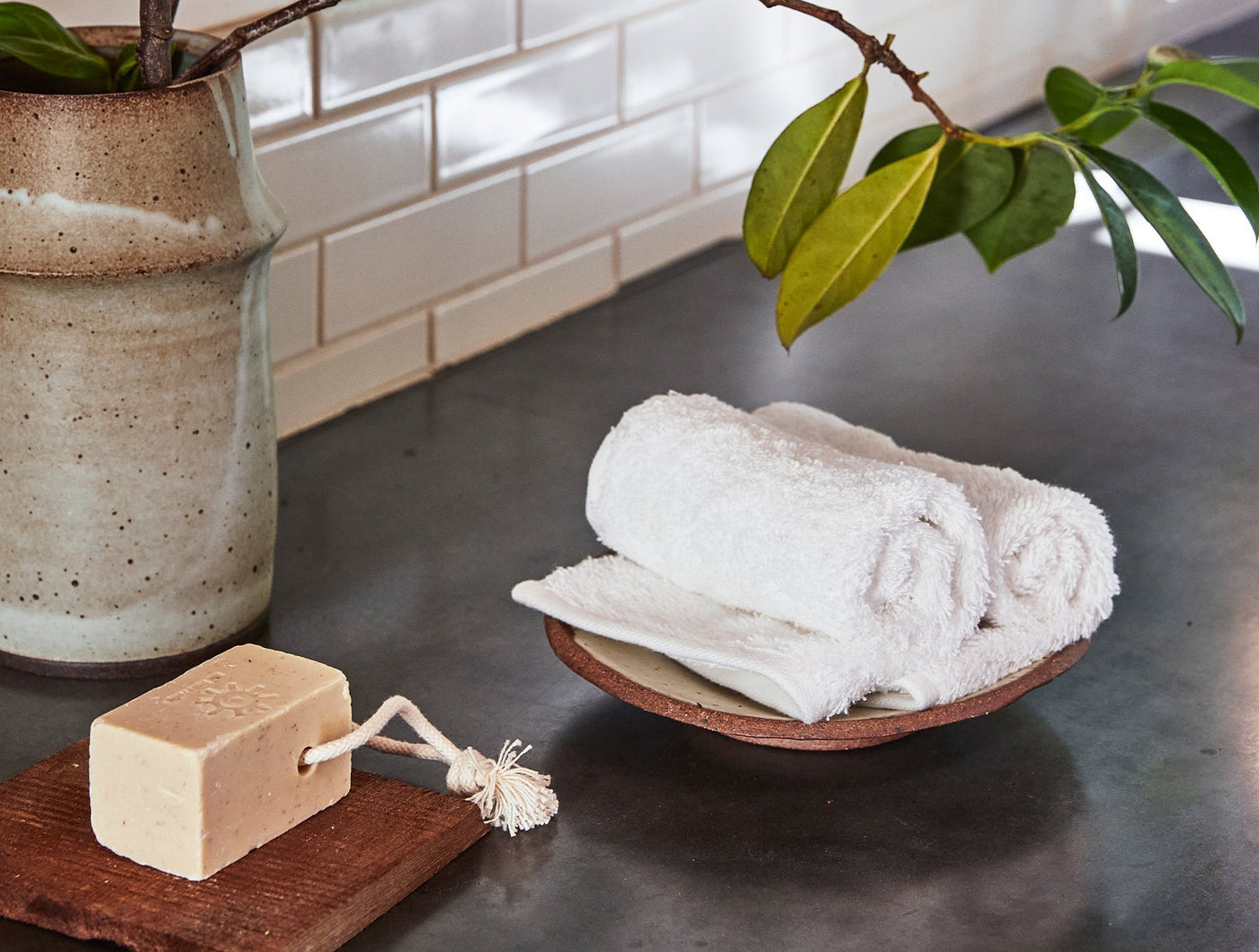 White Coyuchi Cloud Loom wash cloths rolled in a terracotta dish, bathroom counter styling.