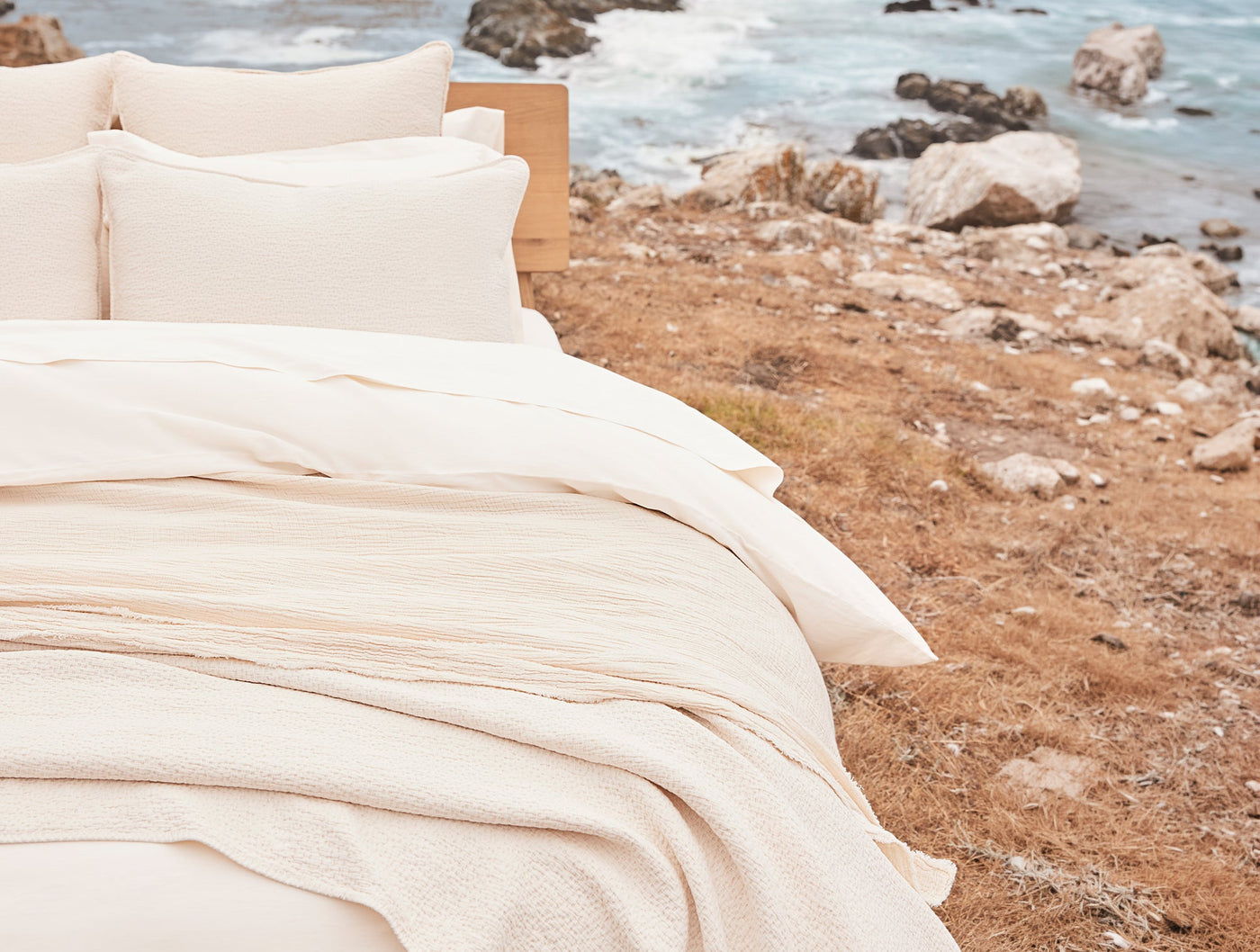 Ivory matelasse blanket draped over a coastal outdoor bed scene.
