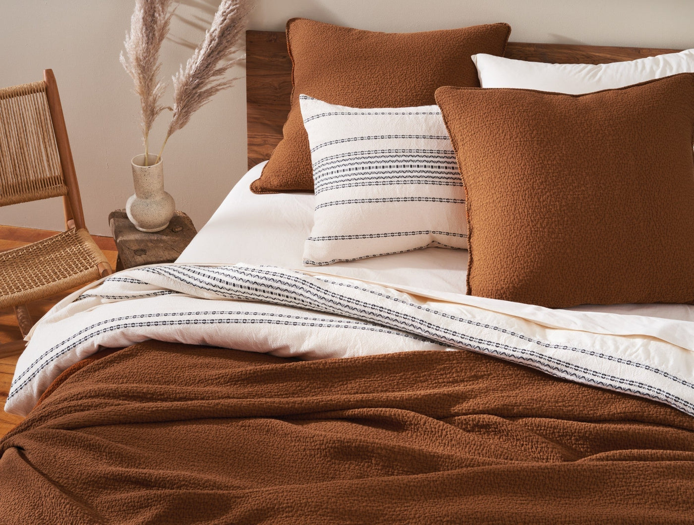 Ivory duvet with indigo rippled stripe detail, styled with rust boucle pillows on a wood bed.