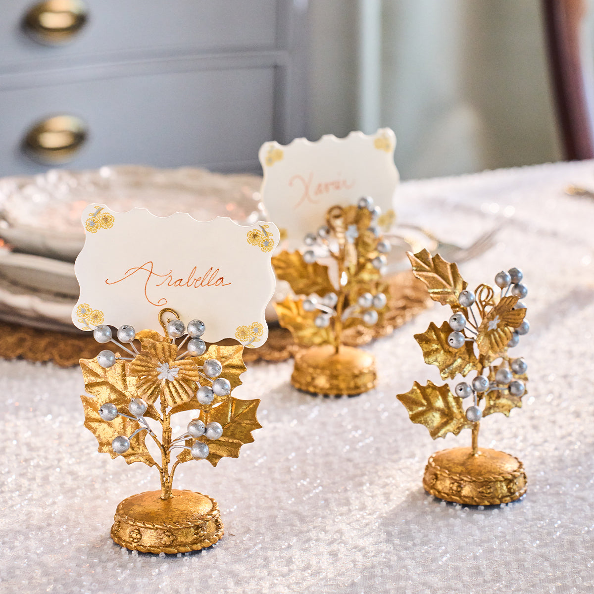Gold holly place card holders with handwritten scalloped cards on a white table setting