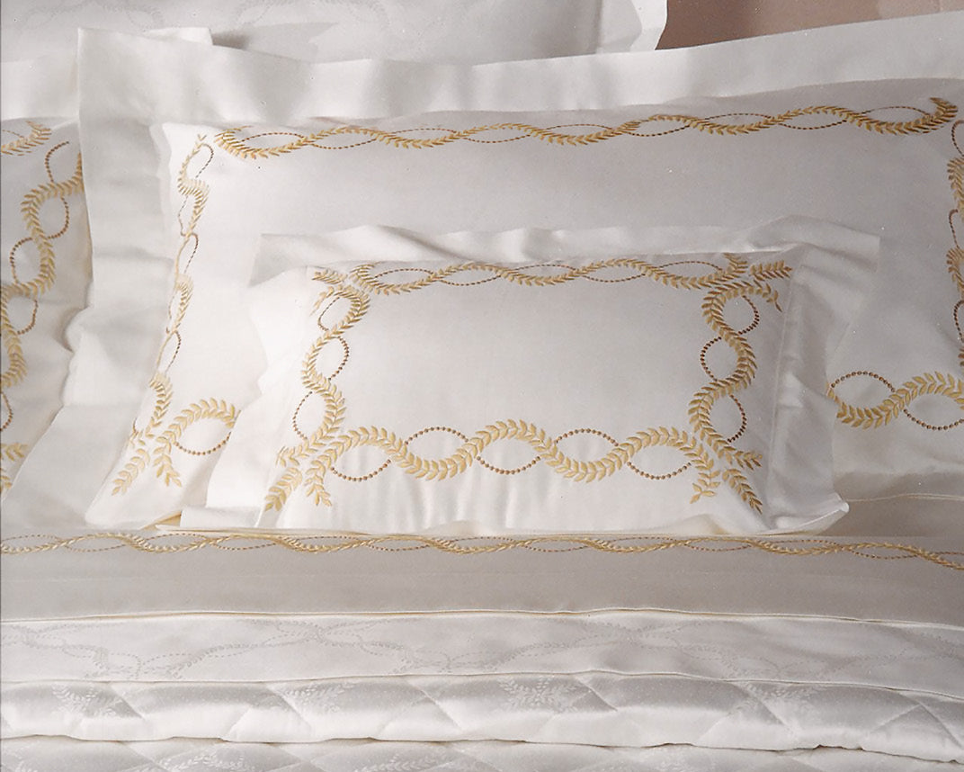 Elegant white bedding set featuring decorative gold embroidered patterns on pillows and a quilt. Soft and luxurious appearance.