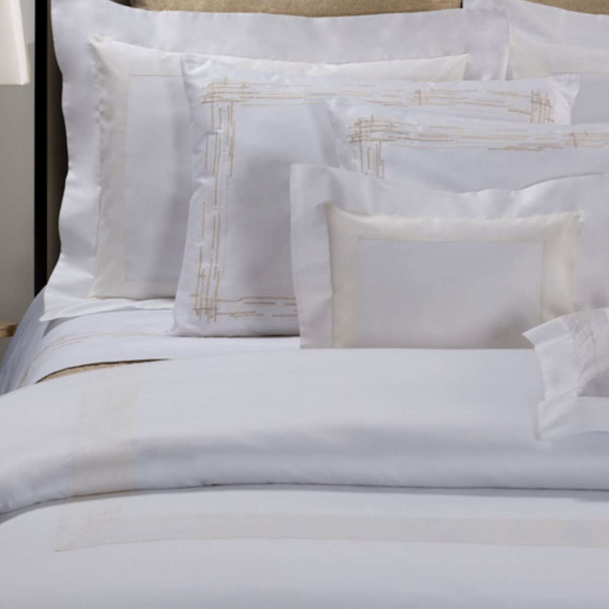 White bed linens with gold embroidery on a bed.