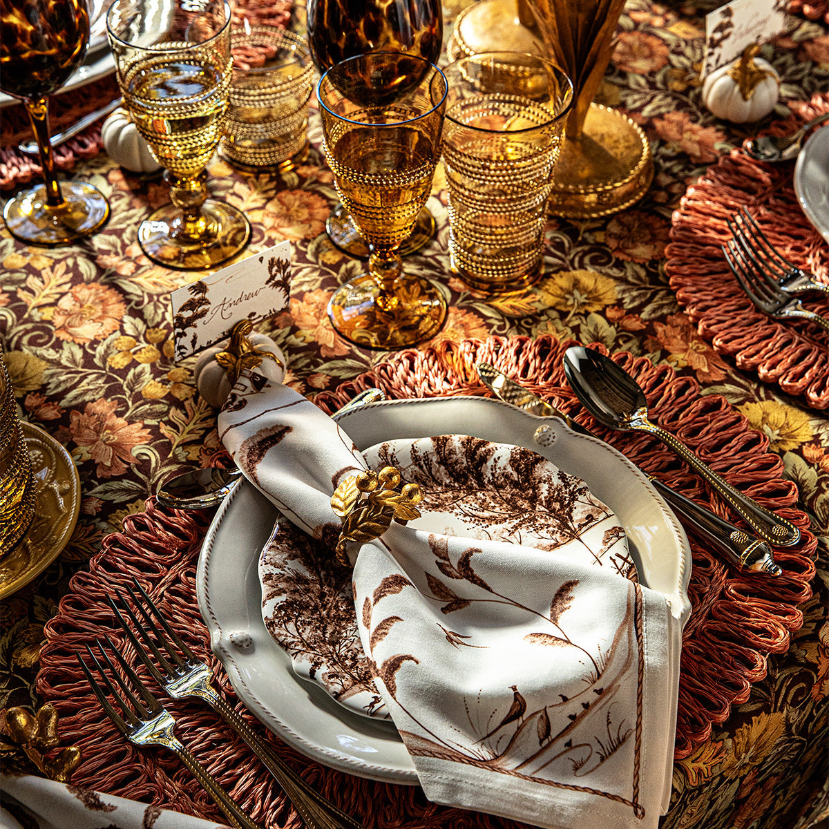 Gold leaf napkin ring on a printed napkin at a place setting with amber glassware