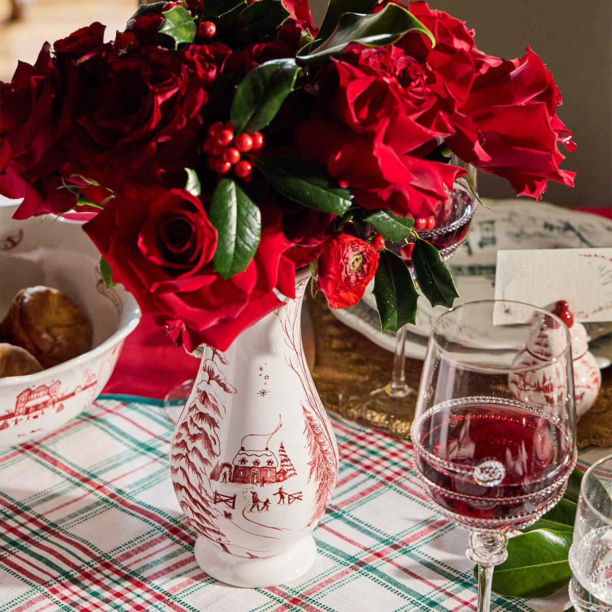 Ruby Winter Frolic vase filled with red roses and holly on a plaid tablecloth