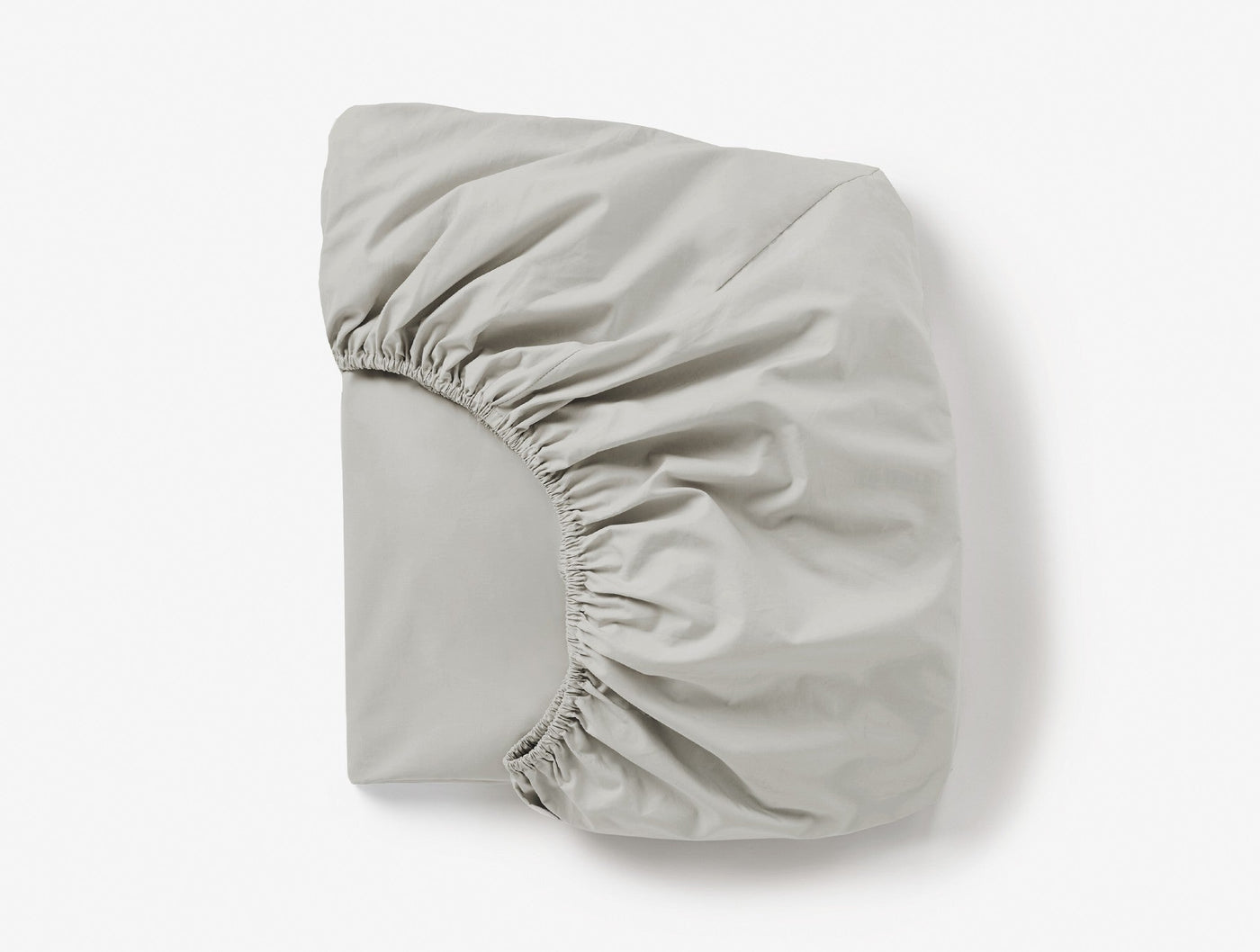 Coyuchi Refined Percale fitted sheet folded, showing elasticated corners in pale silver-grey.