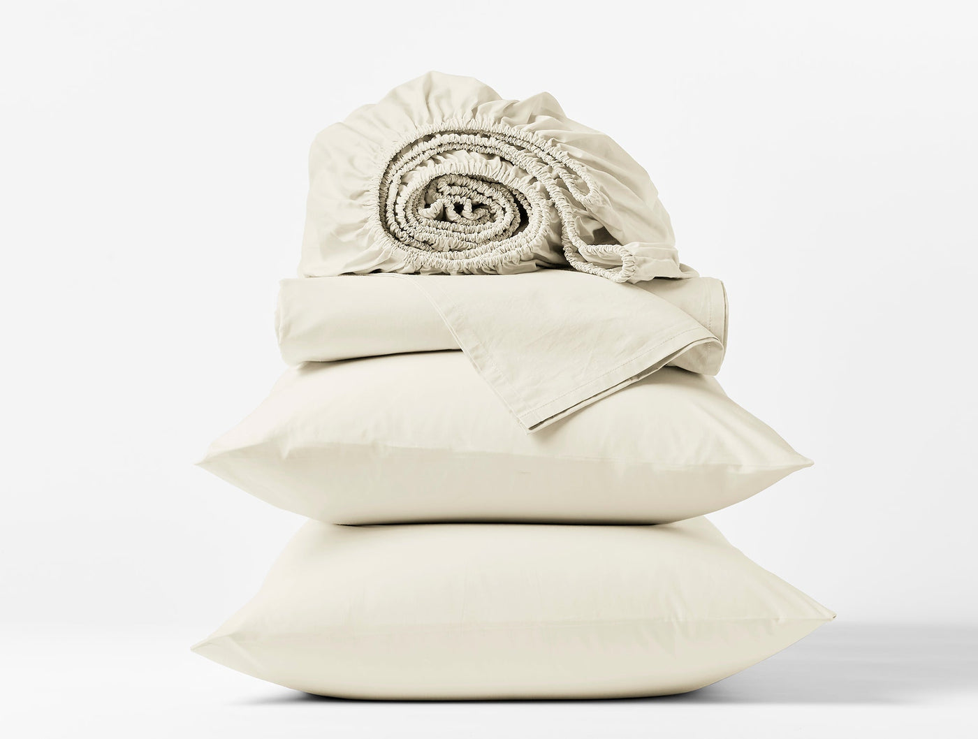 Close-up of stacked ivory Coyuchi Refined Percale pillowcases and rolled fitted sheet.