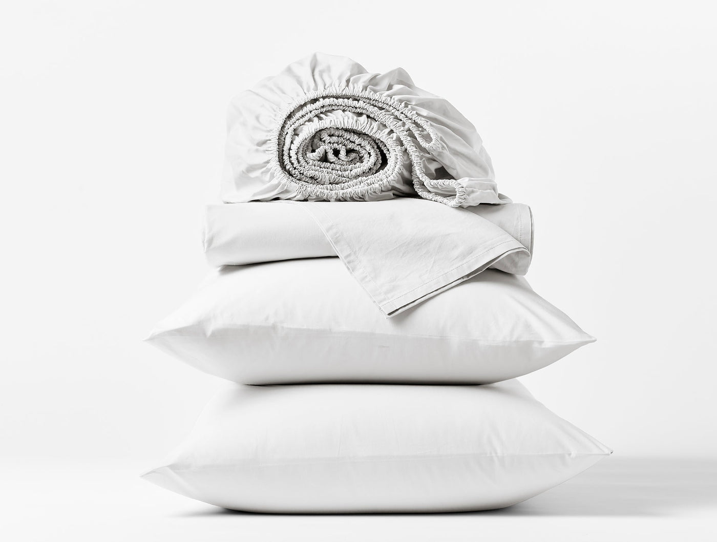 Coyuchi Heritage Percale sheet set in white, stacked pillowcases with rolled fitted sheet on top.