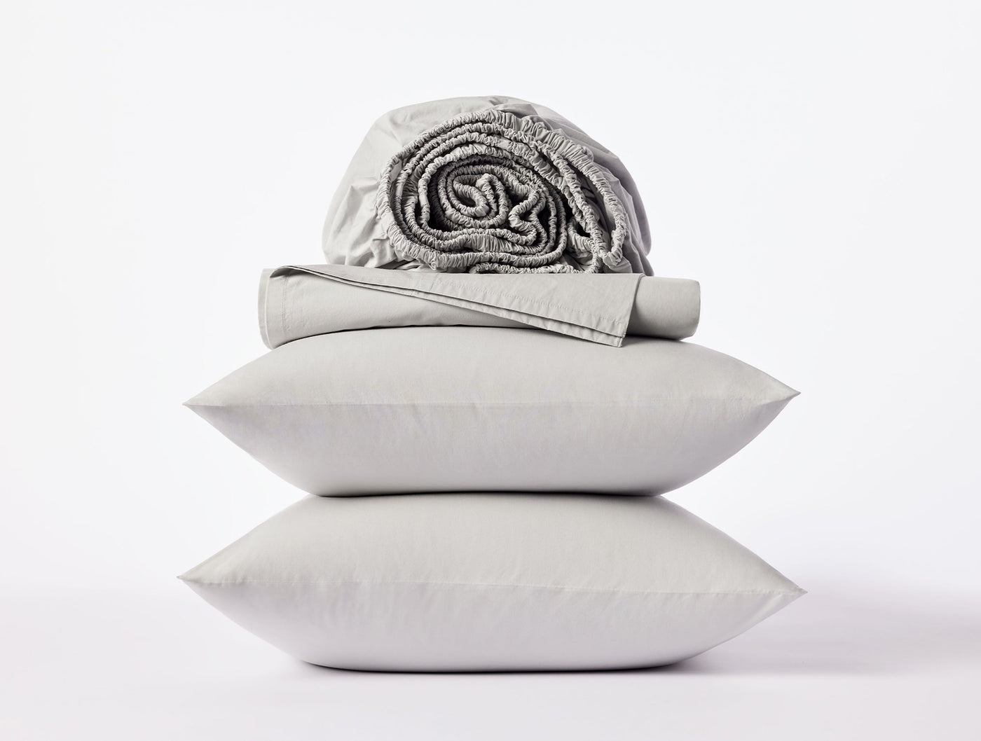 Stacked silver pillowcases with folded and rolled percale sheets on white background.