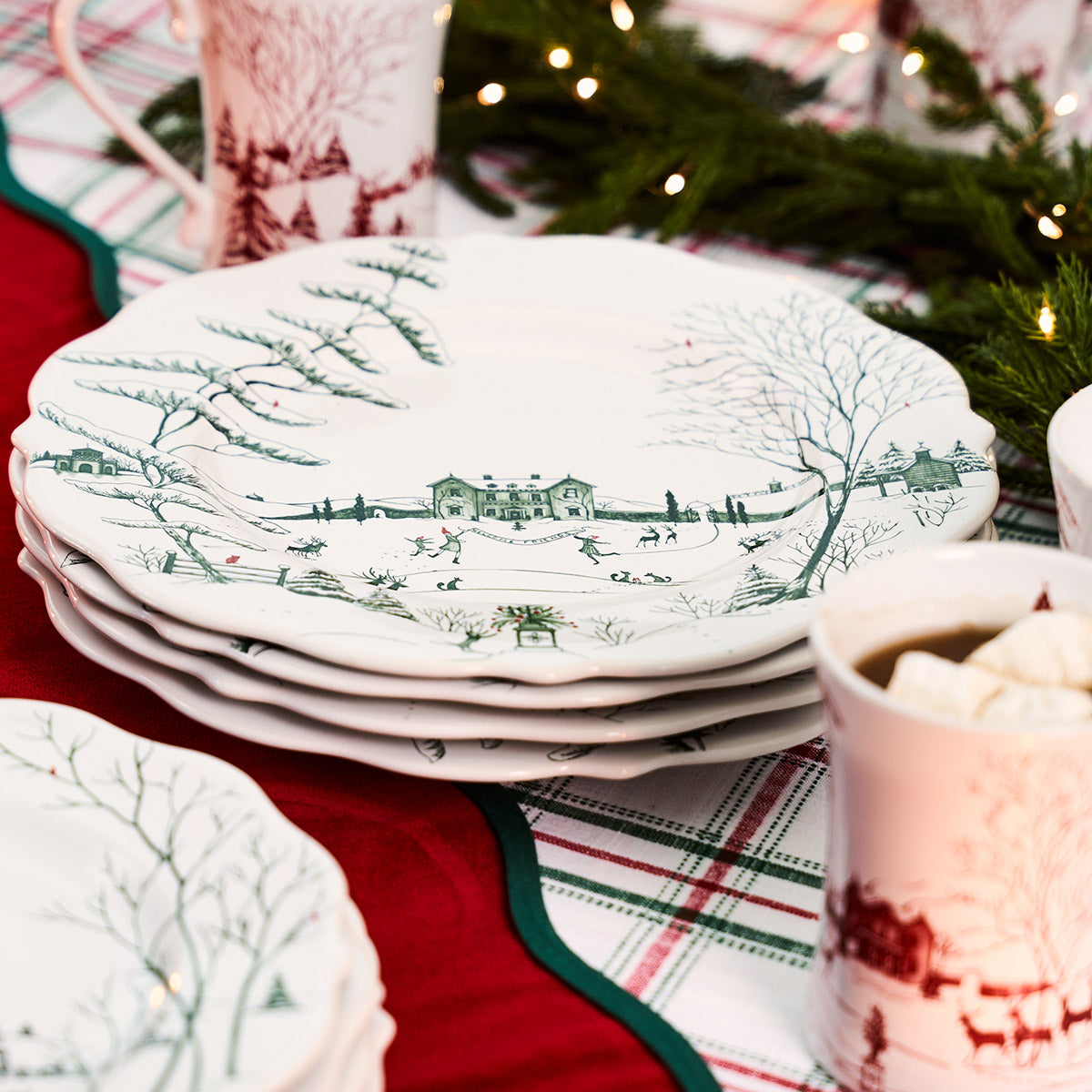 Stack of evergreen Winter Frolic dinner plates on a red and plaid tablecloth