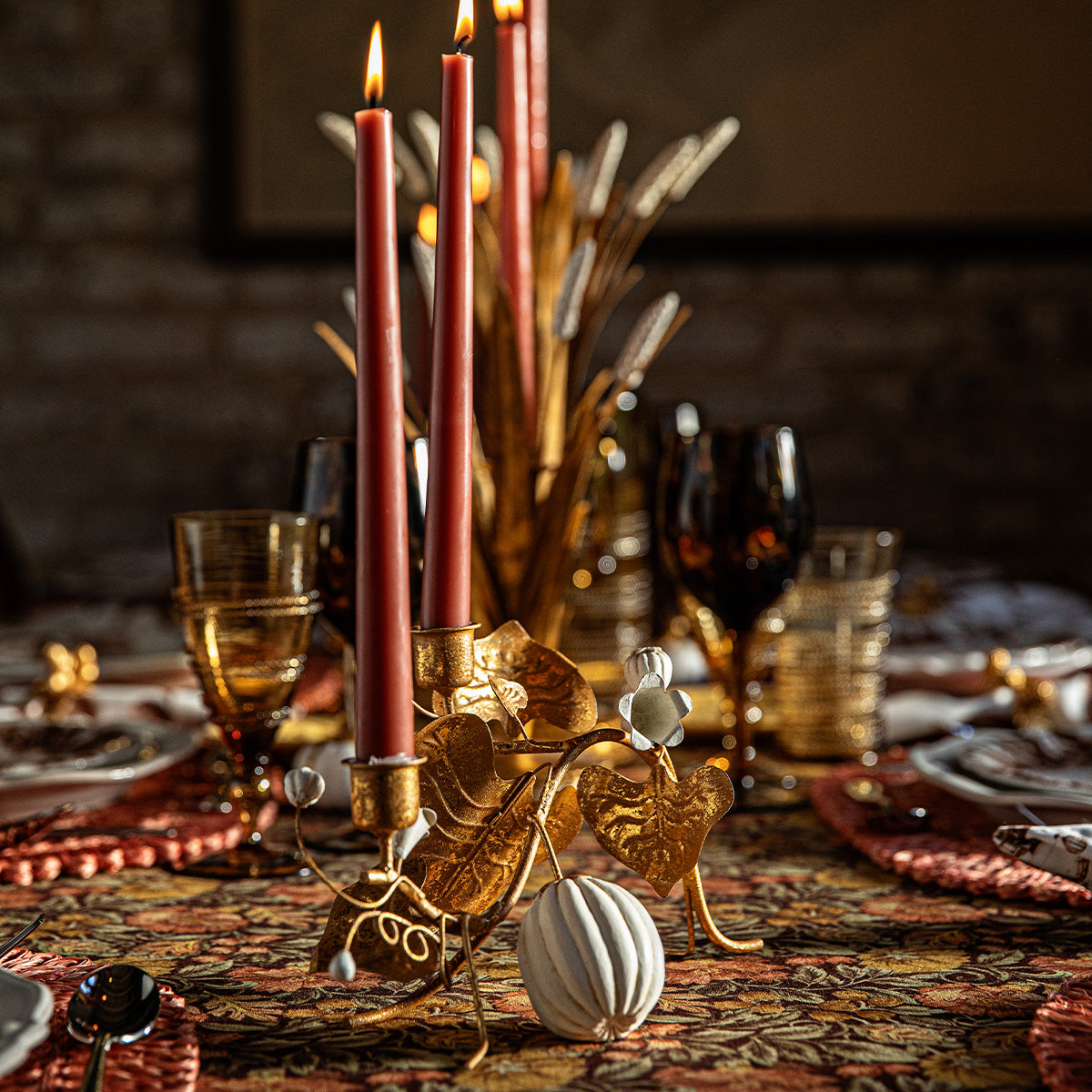 Forest Walk gold pumpkin and vine double candlestick holder with red tapers beside gold wheat on a dark table