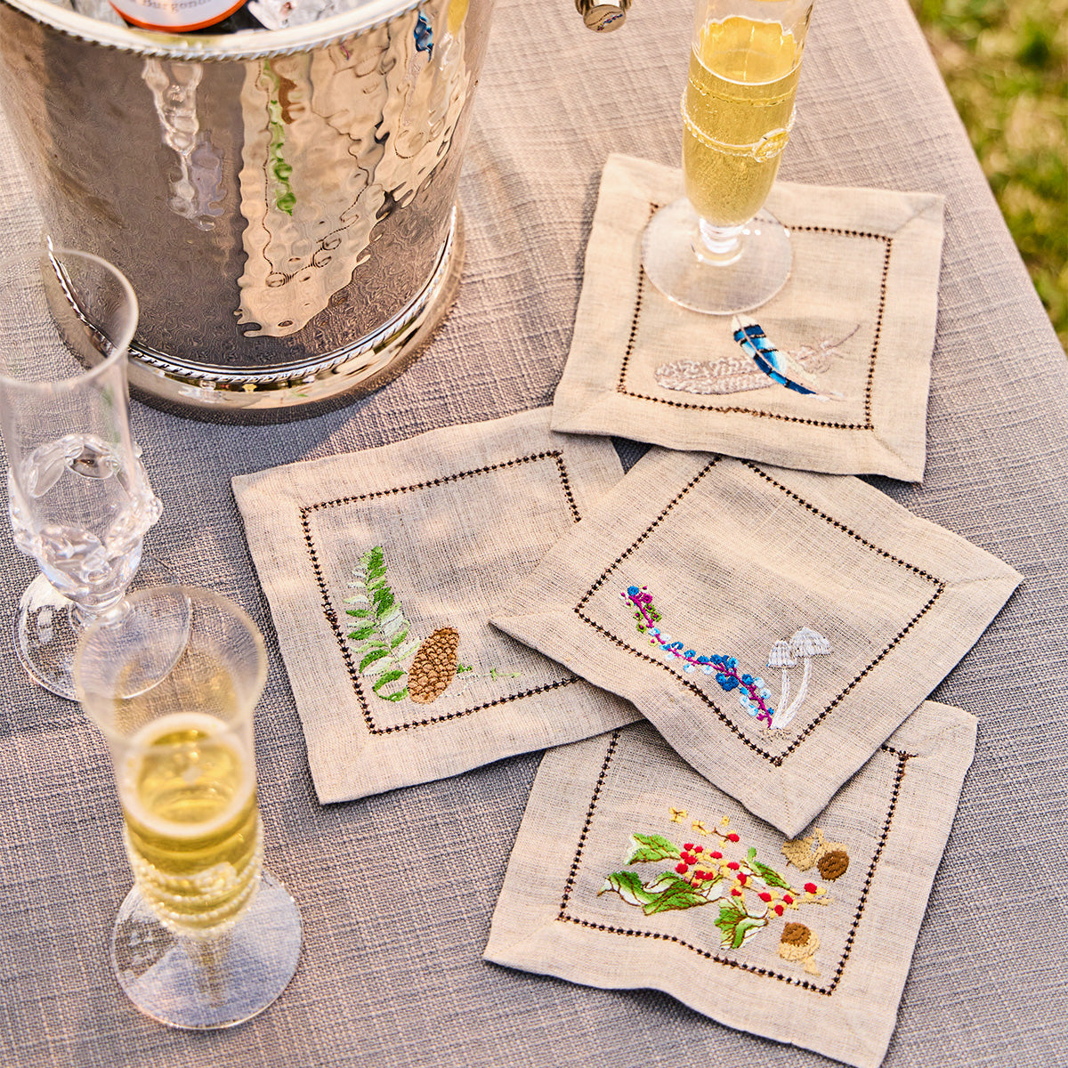 Forest Walk linen cocktail napkins with champagne flutes on a table beside a silver ice bucket