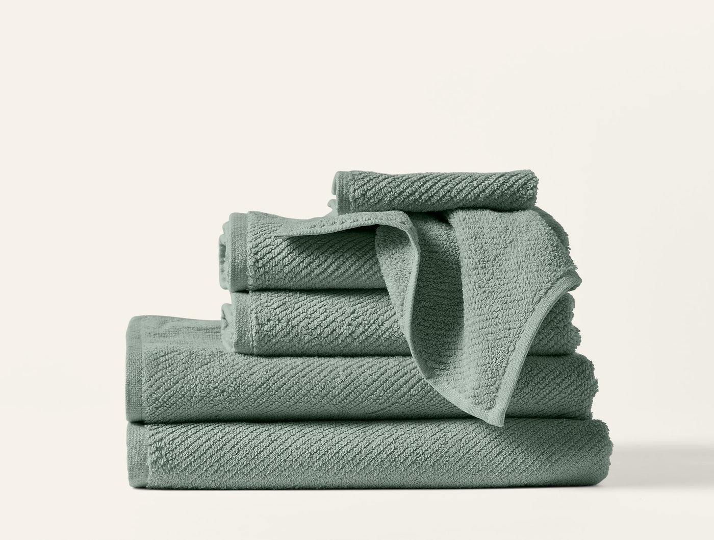 Sage green Coyuchi Air Weight towels stacked, showing textured weave detail.