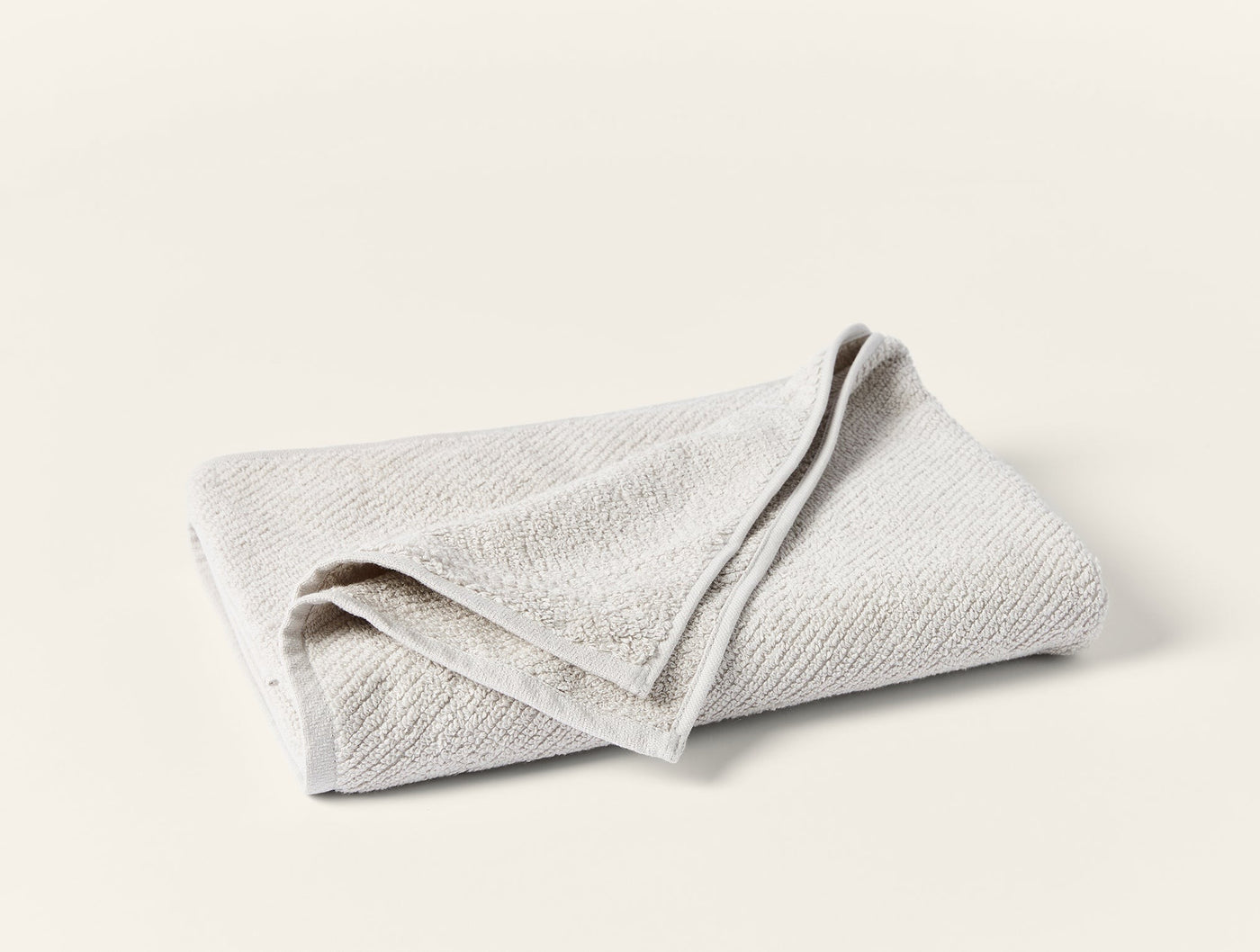 Folded ivory Coyuchi Air Weight guest towel showing subtle textured weave pattern.