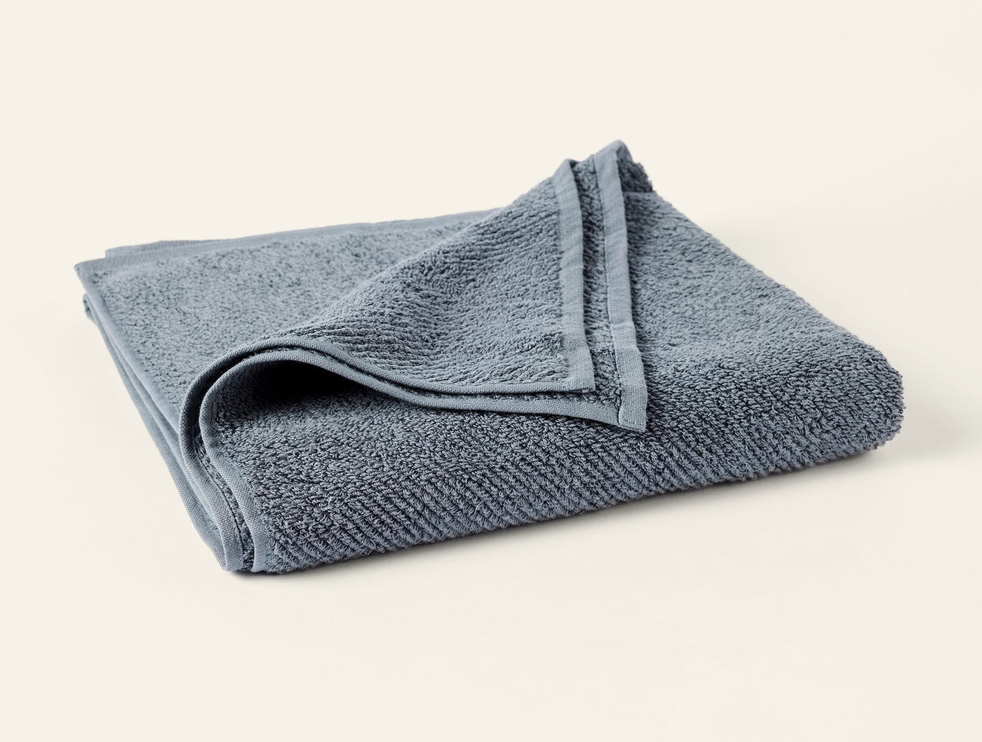 Folded slate blue Coyuchi Air Weight guest towel showing ribbed terry texture and hem detail.