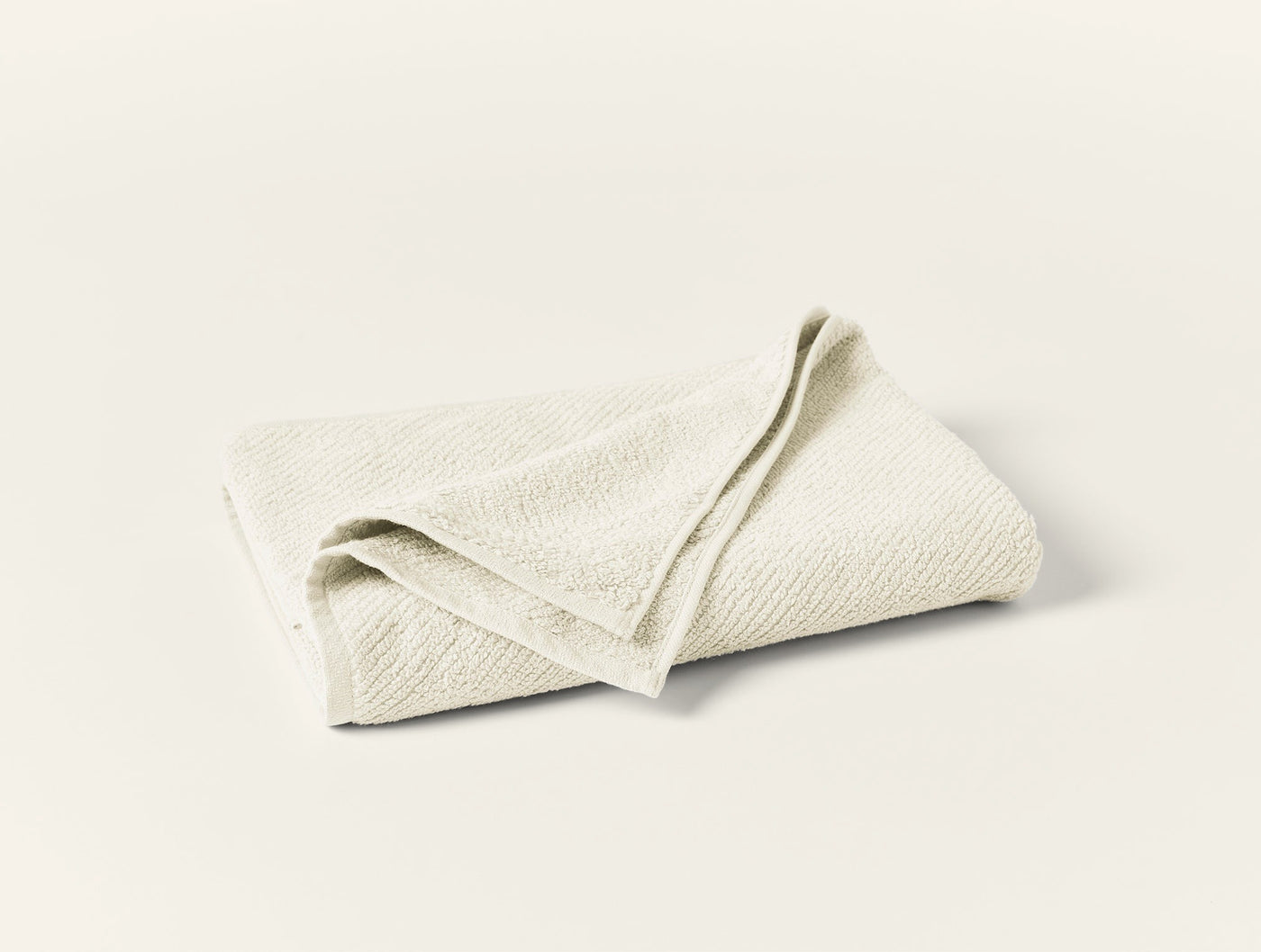 Folded ivory Coyuchi Air Weight guest towel showing subtle woven texture.