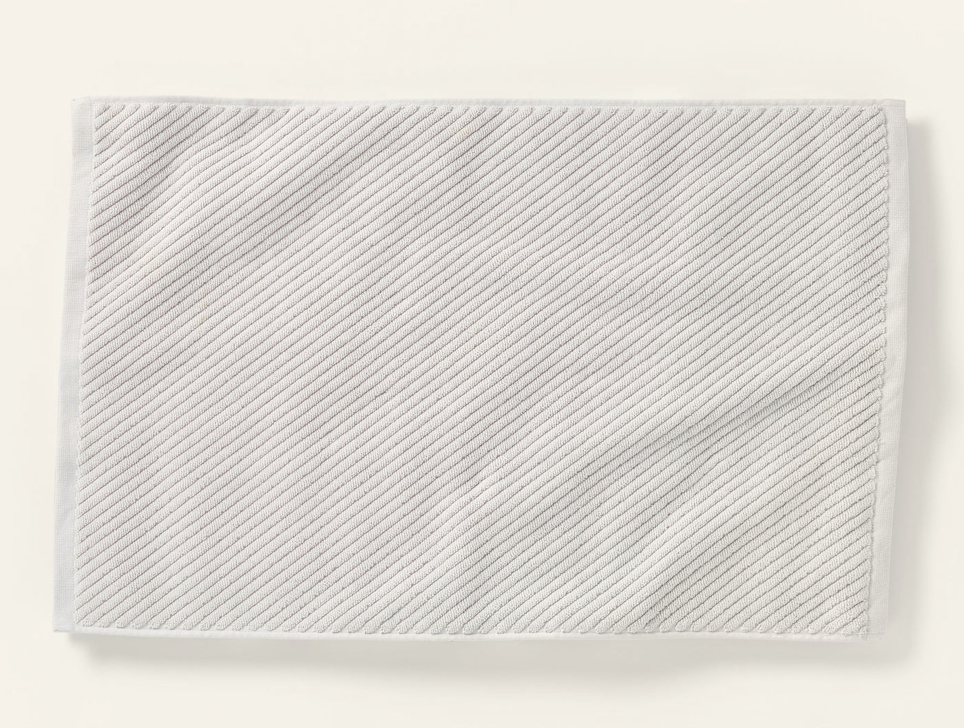Coyuchi Air Weight bath rug laid flat, showing diagonal twill weave texture in white.