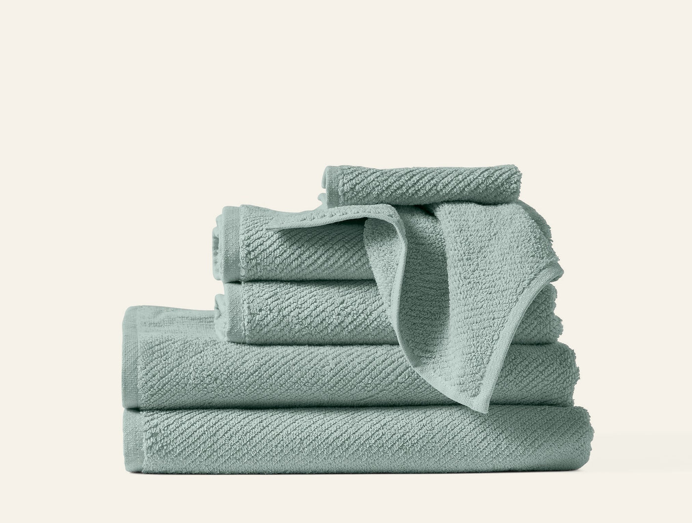 Stacked sage green Coyuchi Air Weight towels showing varied sizes and textured weave.