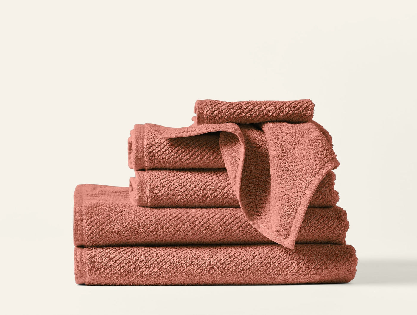 Close-up stack of six Coyuchi Air Weight wash cloths in terracotta with ribbed texture.