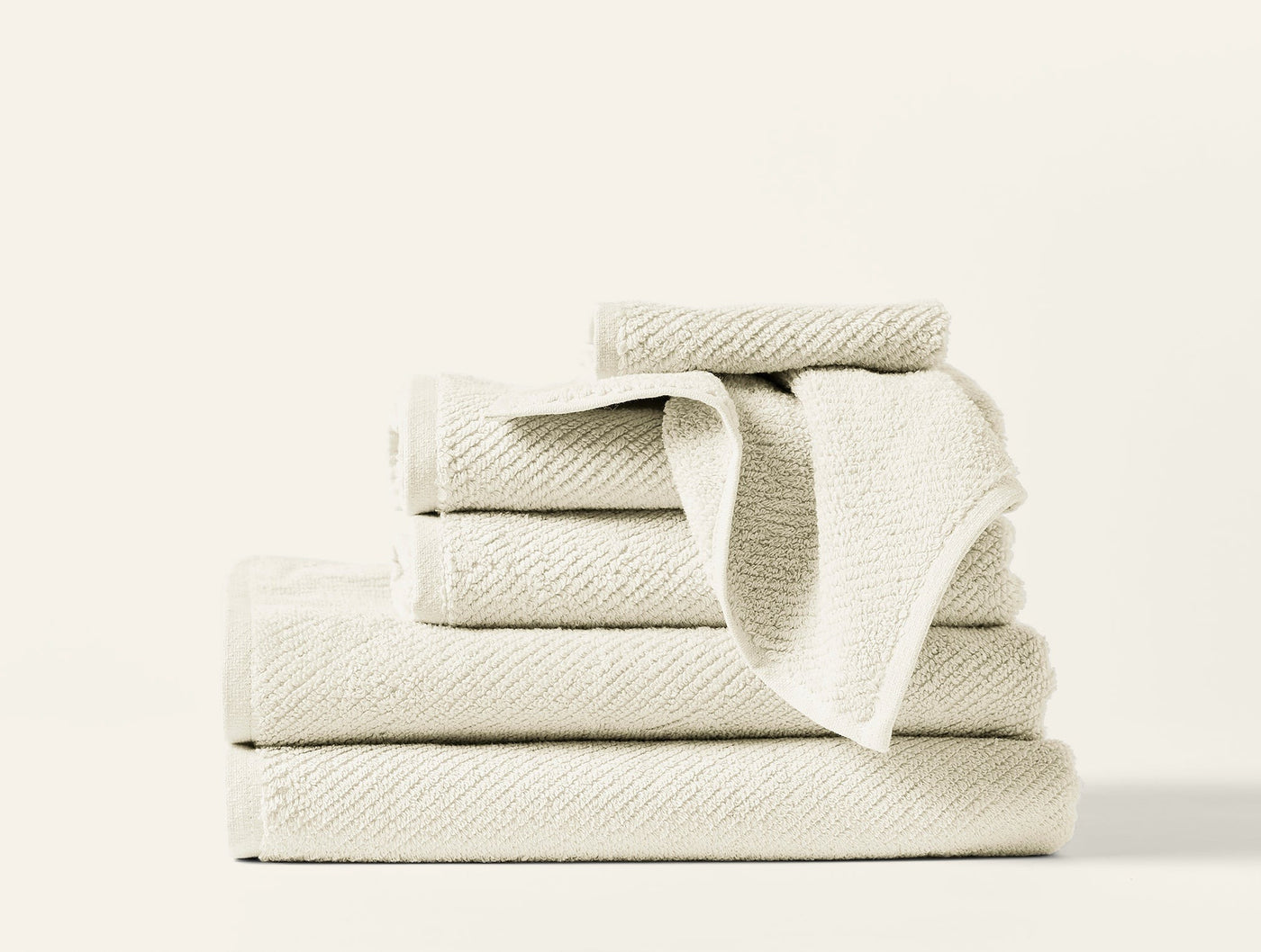 Stacked ivory Coyuchi Air Weight towel set showing varied sizes with ribbed texture detail.