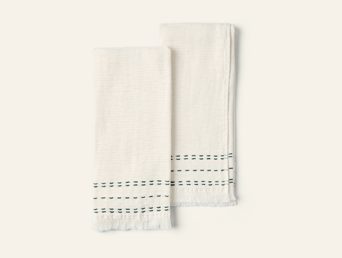 Pair of ivory hand towels with green dashed stripe detail and fringe hem, flat lay view.