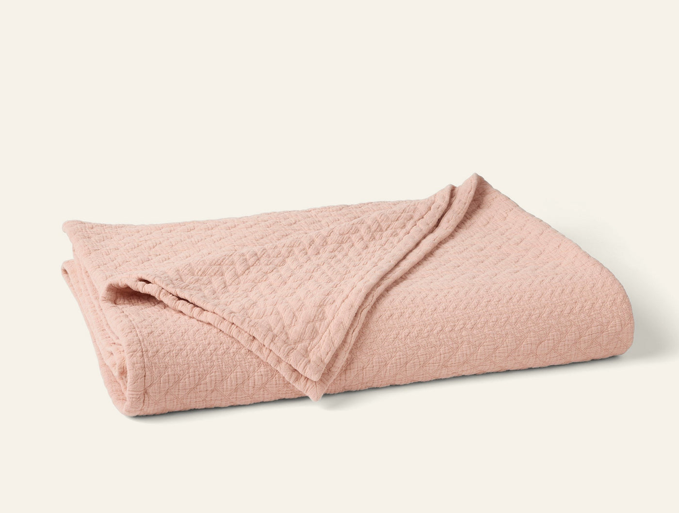 Coyuchi Angeles Matelassé blanket folded, showing blush cotton texture and diamond weave pattern.