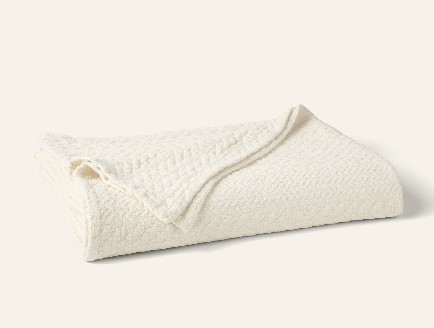 Close-up of folded ivory Coyuchi Angeles Matelasse blanket showing textured weave detail.