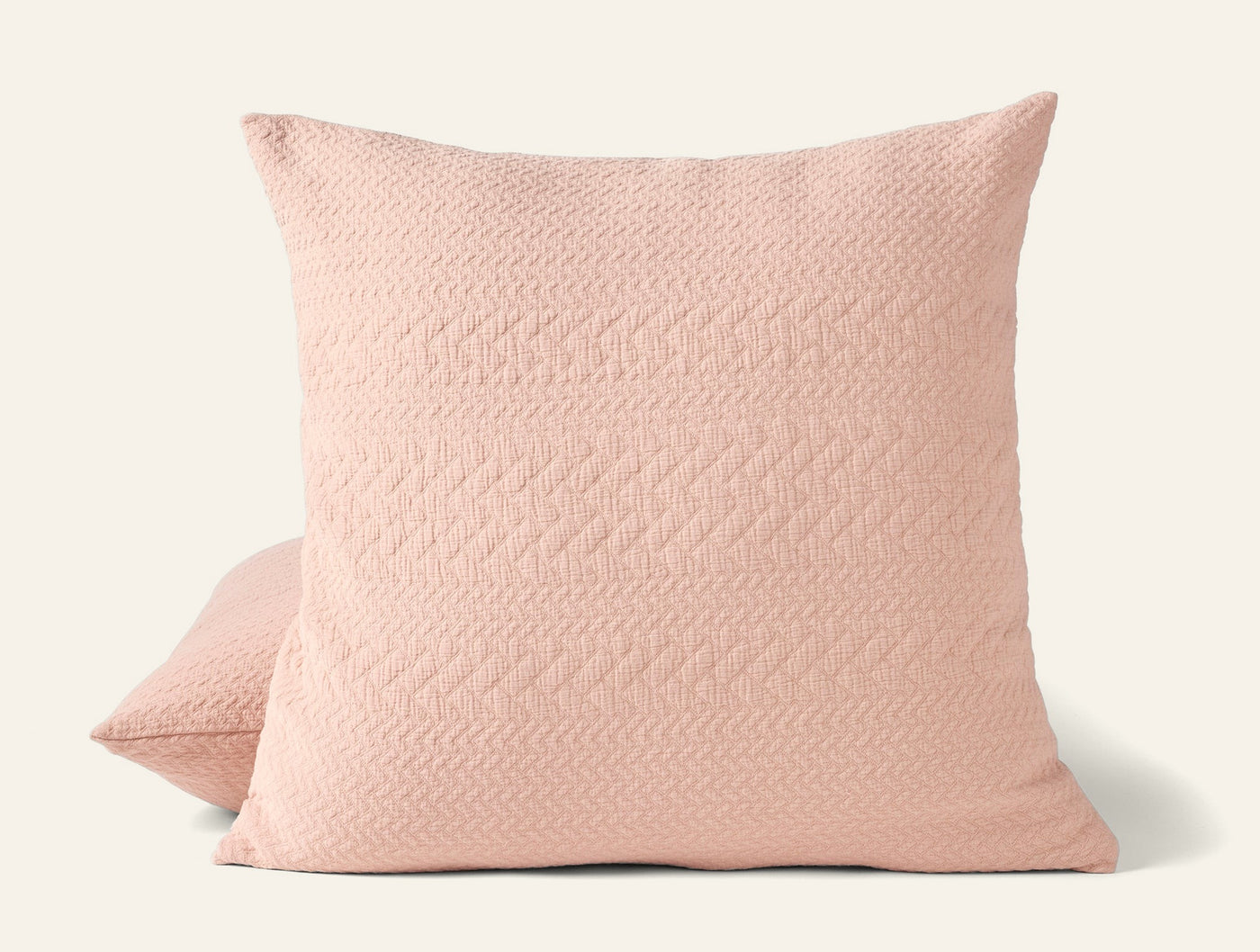 Blush pink matelassé pillow sham with subtle herringbone texture, shown front and side.