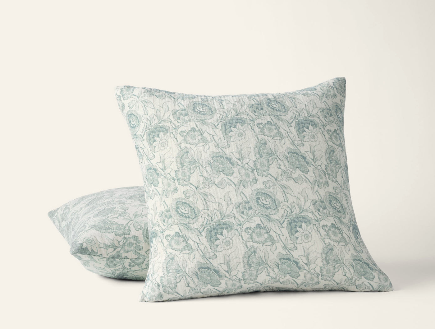Two Coyuchi Balboa Matelassé pillows, ivory with sage floral print, stacked at an angle.