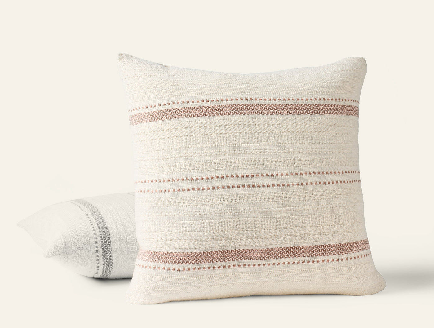 Two Coyuchi Bonita pillows stacked, ivory cotton with dusty rose woven stripe detail.
