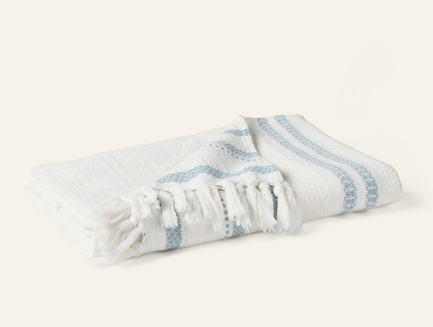 Coyuchi Bonita throw in white with dusty blue woven stripes and fringe trim, folded.