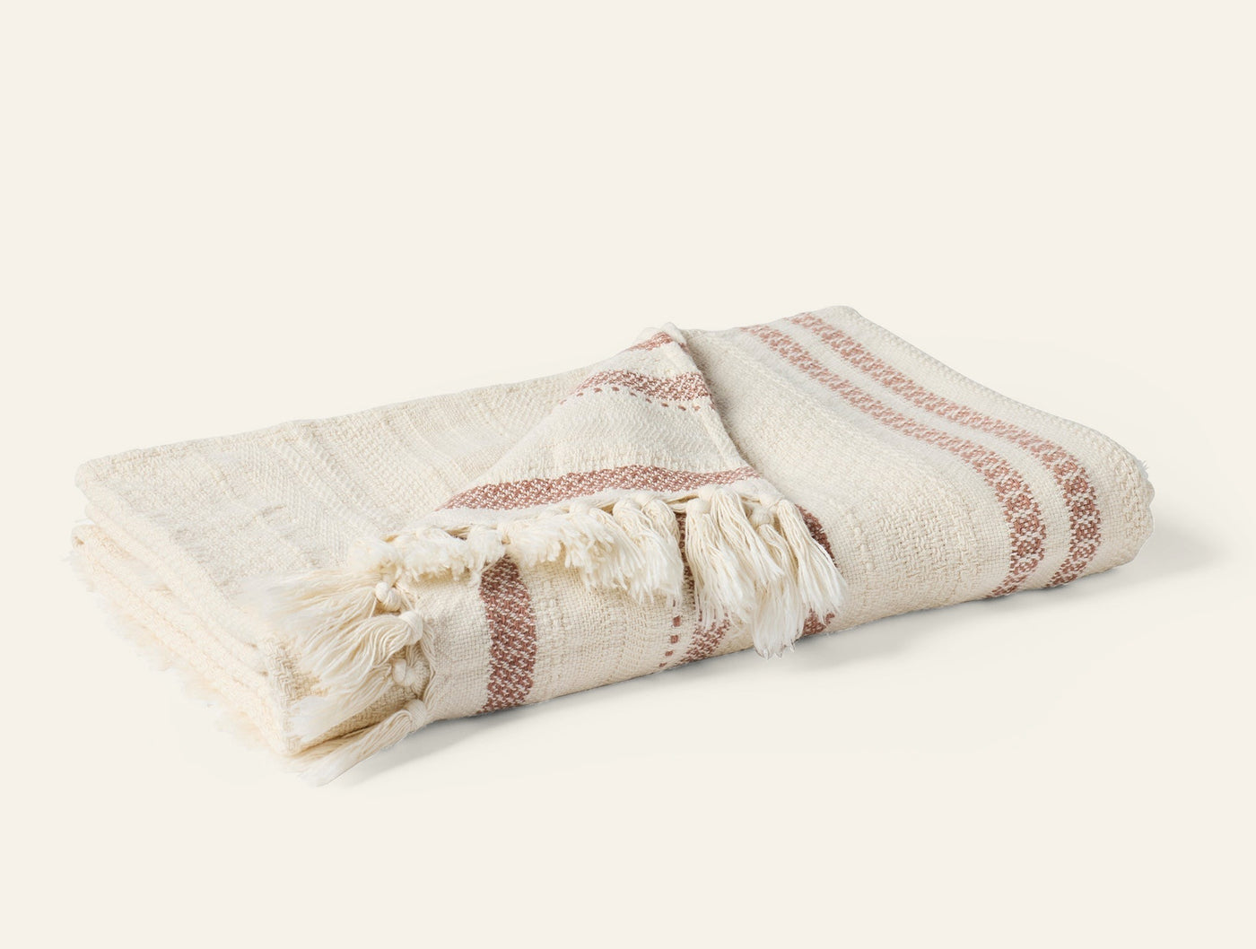 Folded Coyuchi Bonita throw in ivory with terracotta stripe detail and fringe trim.