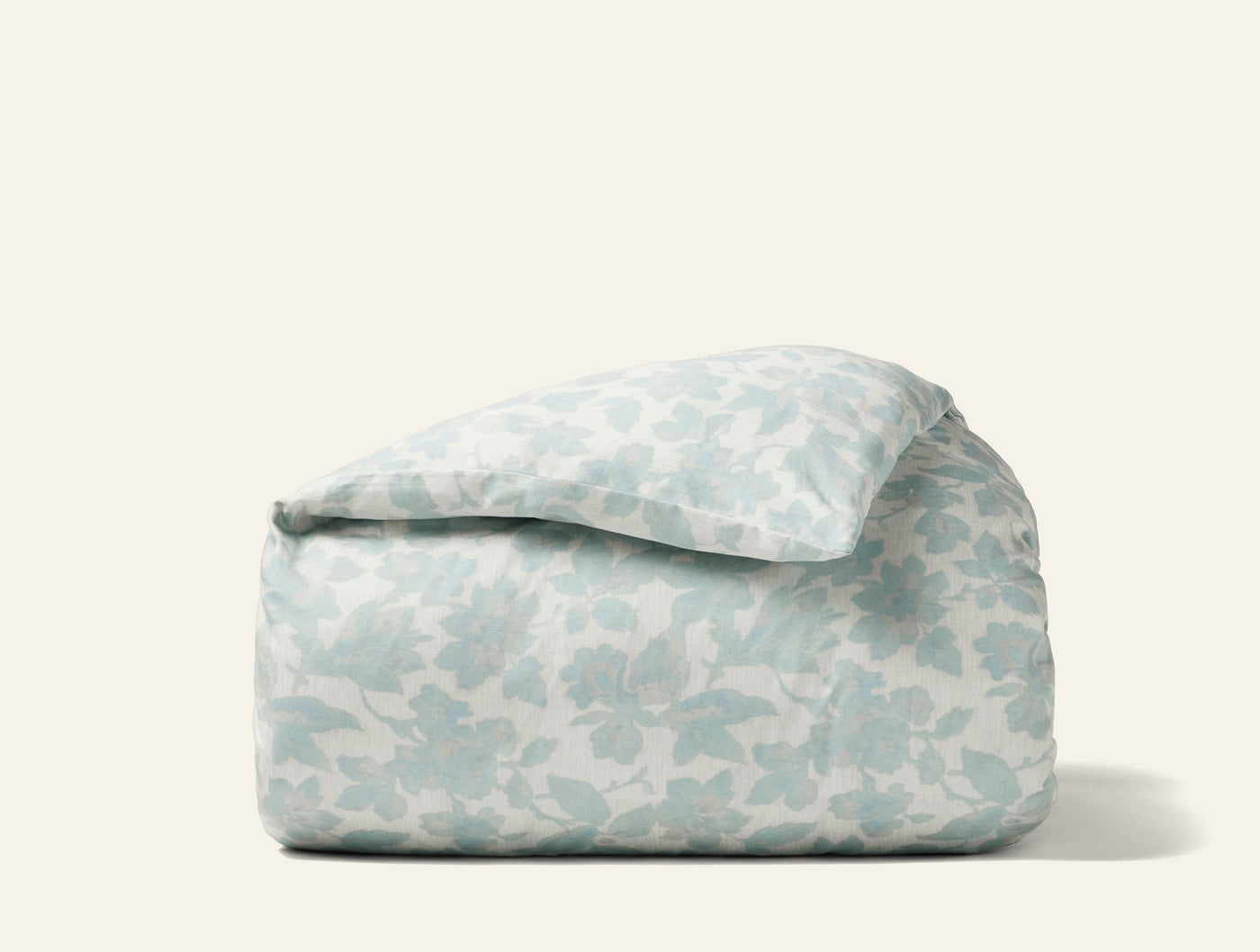 Coyuchi Camellia Print duvet cover folded, showing soft blue floral pattern on ivory ground.
