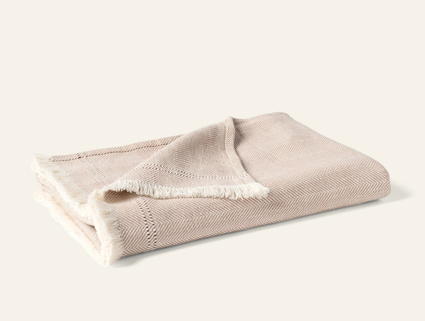Folded Coyuchi Canyon throw in oatmeal herringbone weave with fringe trim detail.