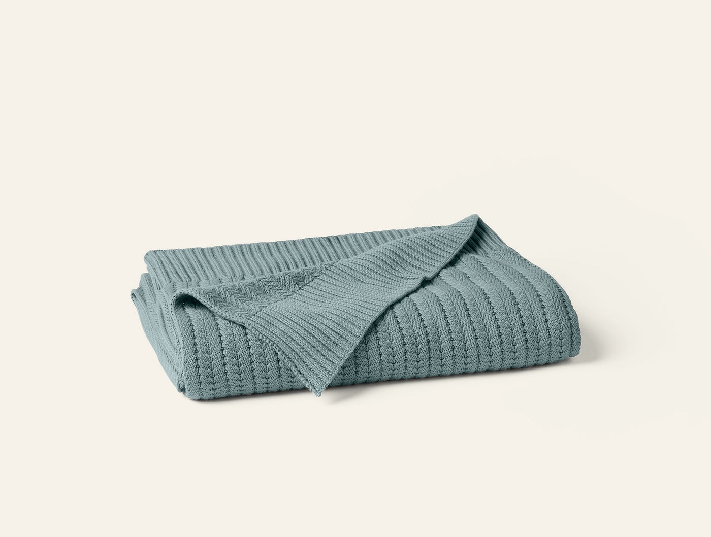 Folded sage green ribbed knit throw, showing textured cable pattern and neatly stacked layers.