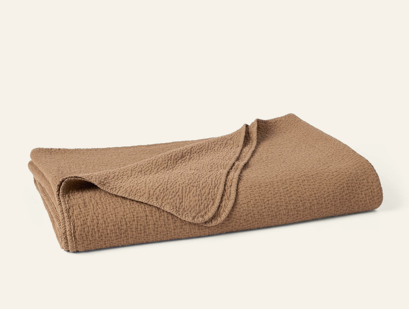 Folded caramel matelassé blanket showing textured weave pattern on rounded corners.