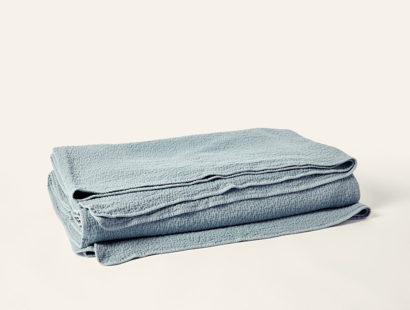 Coyuchi Cascade Matelassé blanket folded, showing seafoam textured weave and scalloped edge.