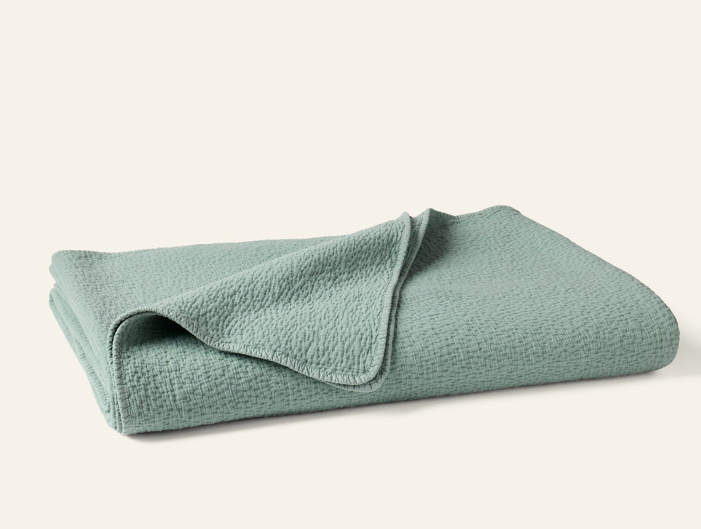 Coyuchi Cascade Matelassé blanket folded, seafoam green with textured weave detail.
