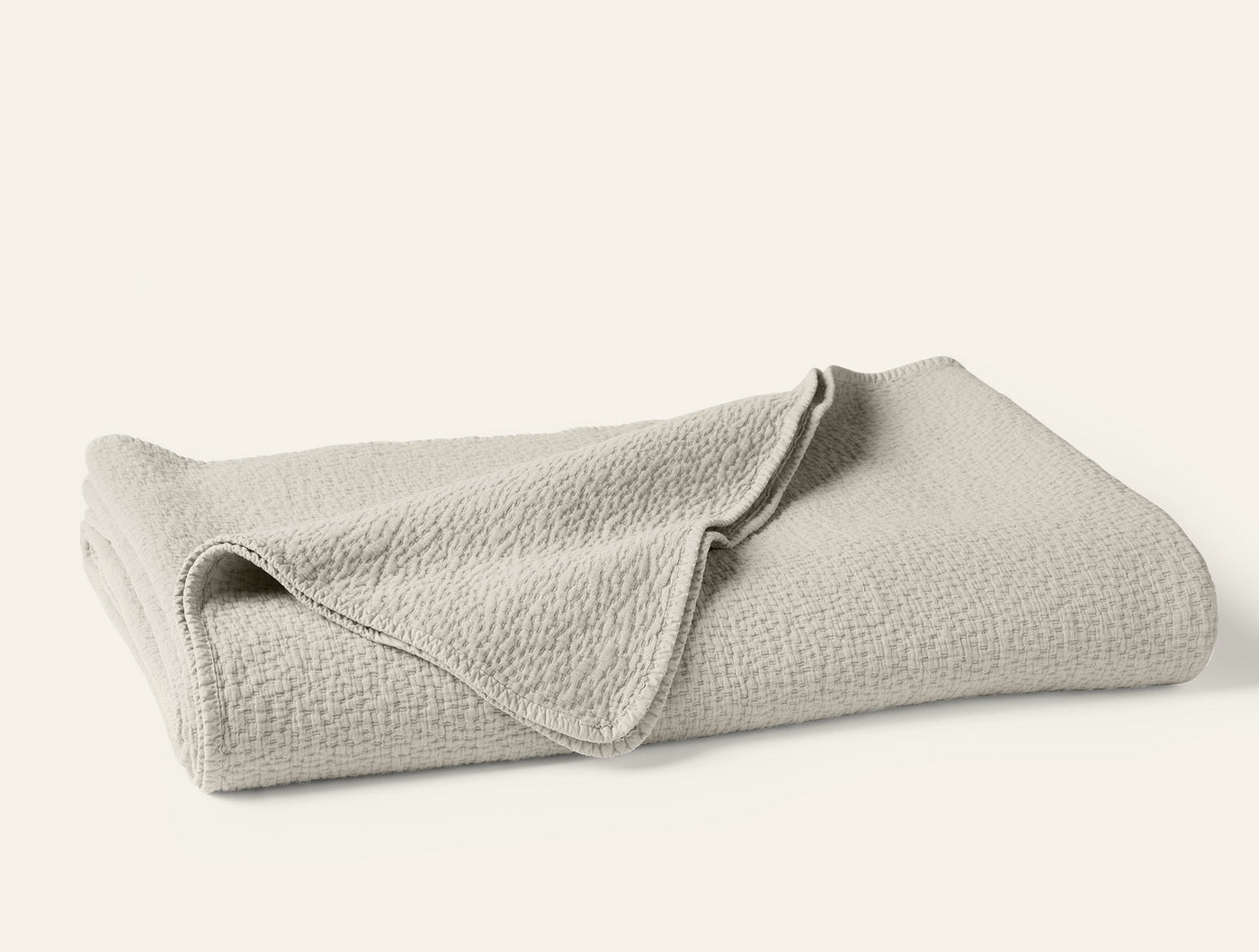 Folded ivory Coyuchi Cascade Matelasse blanket showing textured weave detail.