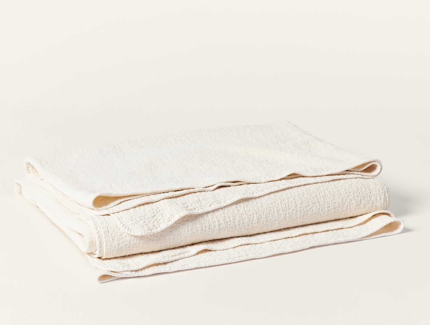 Coyuchi Cascade Matelassé blanket folded, showing ivory textured weave and scalloped edges.