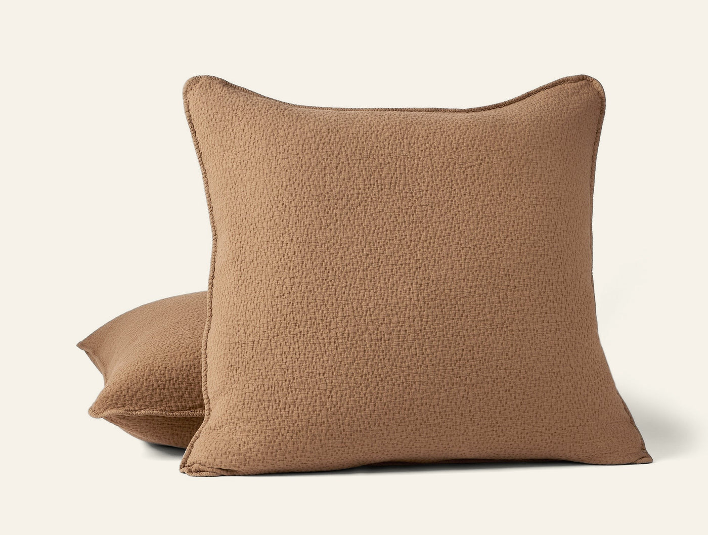 Close-up of two stacked camel matelassé pillow shams with textured weave and contrast trim.