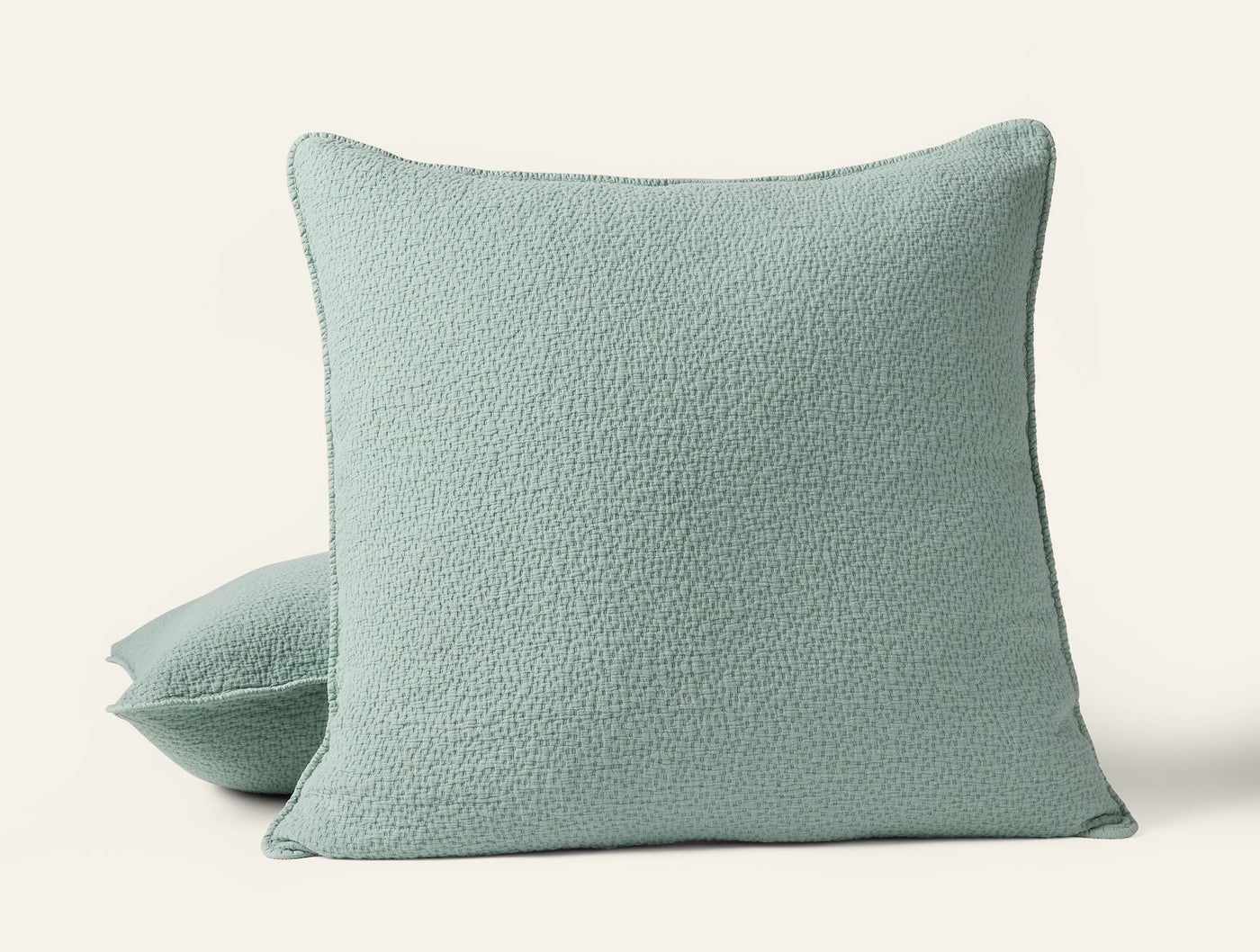 Sage green matelassé pillow sham with subtle textured surface, shown with stacked second sham.