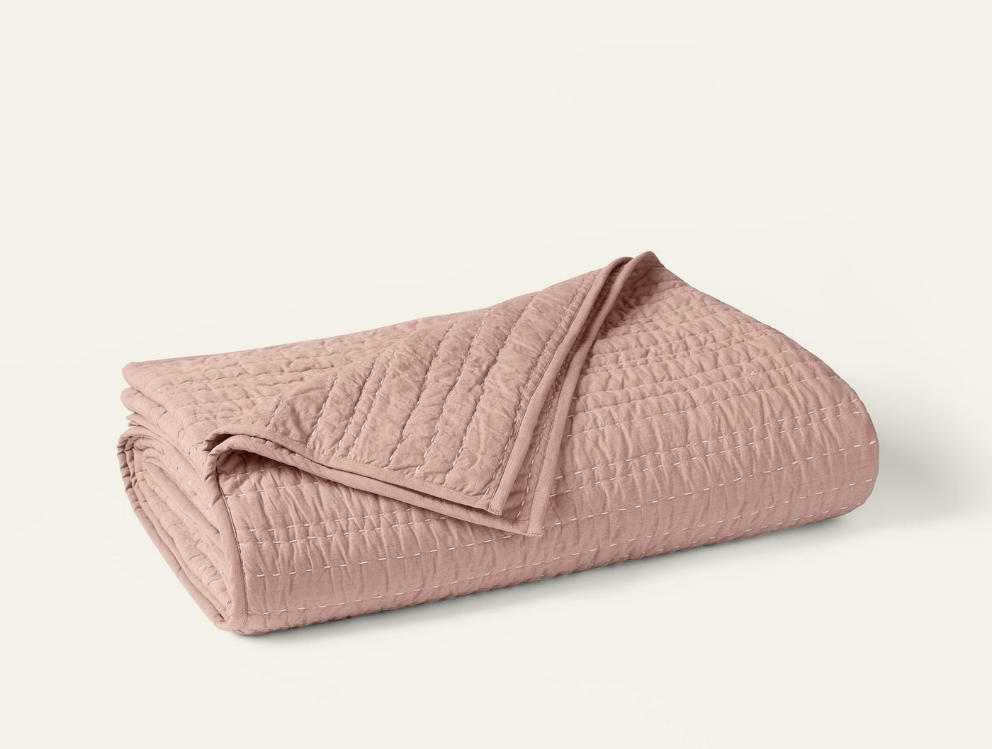 Coyuchi Channel Handstitched quilt folded, showing rose blush tone and quilted channel texture.
